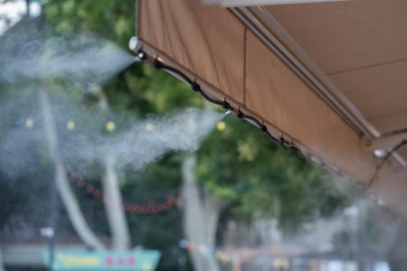 Automatic mist nozzle water spraying system to make humidifier and cooling climate to reduce hot weather. Water fog machine working during hot summer day. Refreshes plants and cleaning air outdoors